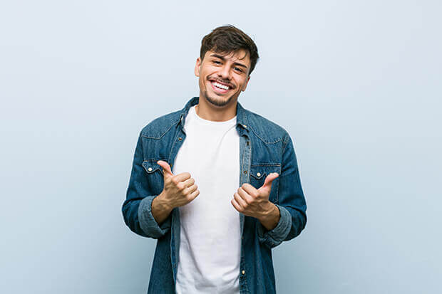 A smiling Latino man holding two thumbs up